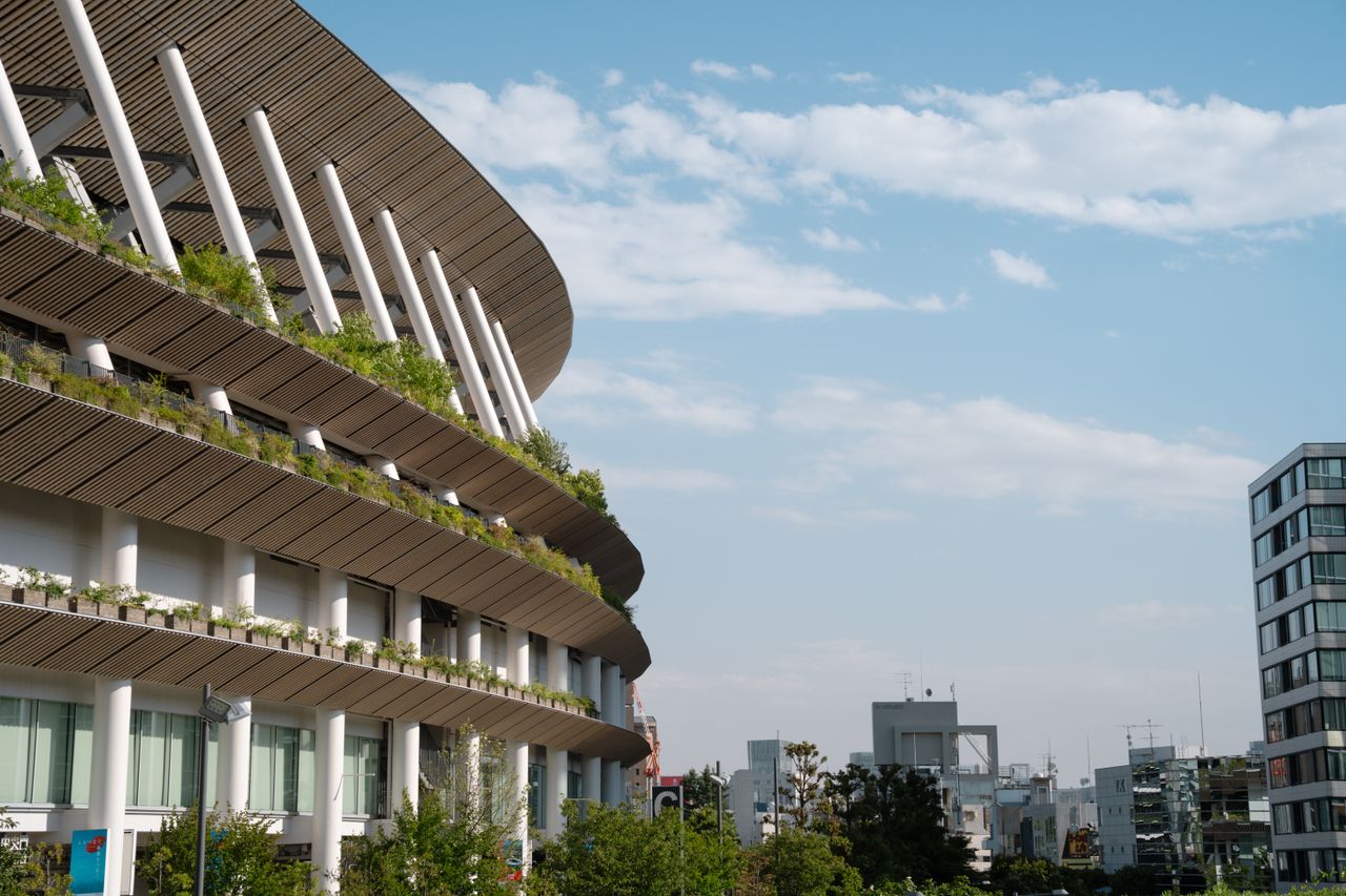A striking view of Tokyo National Stadium featuring greenery and modern design against a clear sky.